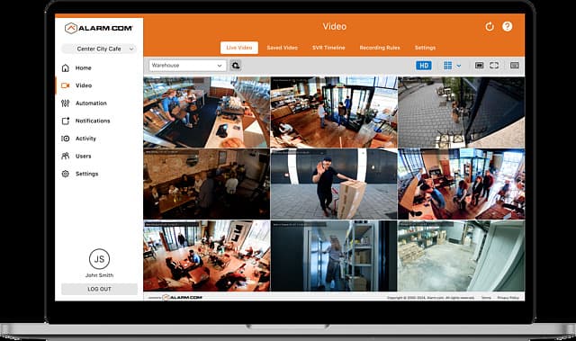 The Alarm.com web dashboard on a laptop, showing nine live camera feeds across a café and warehouse